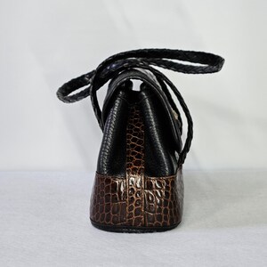 May include: A black and brown handbag with a braided handle. The top portion is black, while the bottom is brown with a crocodile pattern. The bag has a flap closure and a gold-colored clasp.