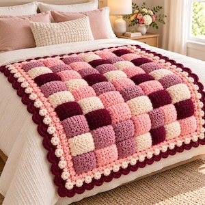 May include: A handmade crochet blanket featuring a textured, three-dimensional puff stitch pattern in a checkerboard arrangement. The blanket displays alternating squares of cream, light pink, mauve, and deep burgundy, finished with a scalloped border.