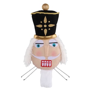 May include: A plush nutcracker head with a black hat adorned with gold accents and a gold trim. The face is beige with blue eyes, a white mustache, and a red mouth. White faux fur forms the hair and beard.