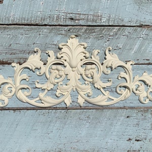 May include: A white, ornate, decorative wall decor piece with a scroll-like design. The piece is made of a lightweight material and has a vintage, antique look.