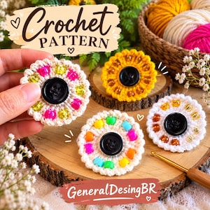 Könnte beinhalten: Vier kreisförmige Häkelblumenmotive mit einem zentralen schwarzen Knopf und einem Ring aus bunten Kunststoffperlen. Die Motive sind aus weißem, gelbem und cremefarbenem Garn gefertigt. Ein Motiv wird gehalten, andere liegen auf einer Holzscheibe.