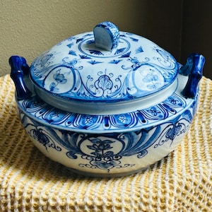 May include: A blue and white ceramic lidded serving bowl with floral and geometric patterns. The bowl has two bamboo-style handles and a small handle on the lid. The design is hand-painted with a traditional aesthetic.