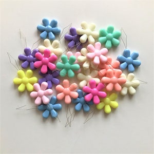 May include: A collection of colorful plastic flower-shaped threaders. The threaders are in various pastel colors, including pink, blue, yellow, green, and purple. Each threader has a small metal loop at the end.