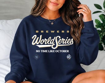 May include: A navy blue crewneck sweatshirt featuring the text "BREWERS WORLD SERIES" in white and gold lettering, with the phrase "NO TIME LIKE OCTOBER" below it, alongside a Brewers logo and a World Series logo on the front.