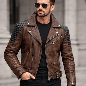 May include: A brown leather motorcycle jacket with black ribbed shoulder panels, silver-tone metal zippers, a wide notched collar, and a waist belt. The jacket is worn over a black t-shirt and black jeans. The text FRONT VIEW is visible.