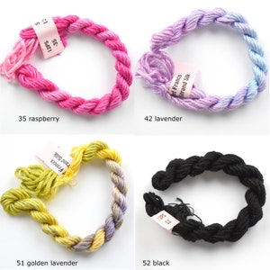 May include: Four spools of embroidery floss in different colors: raspberry, lavender, golden lavender, and black. Each spool has a label with the color name and the brand name "Soft Francis Strand Silk".