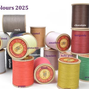 May include: A collection of colorful spools of thread, labeled with various colors like "poppy," "prairie," and "chocolate." The spools are arranged in a visually appealing display, with the text "New Colours 2025" at the top.