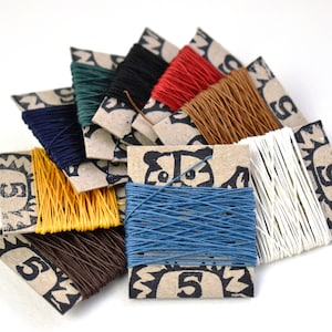 May include: Assortment of colourful waxed cotton threads wound on cardboard spools. Each spool features a raccoon illustration and the number "5".