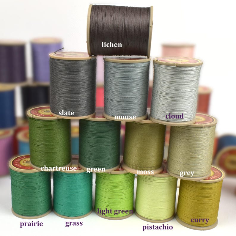 May include: A collection of colorful thread spools in various shades of green, grey, and brown. The spools are labeled with color names such as "lichen", "slate", "mouse", "cloud", "chartreuse", "green", "moss", "grey", "prairie", "grass", "light green", "pistachio", and "curry".