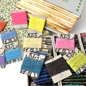 May include: A selection of colourful twine spools in shades like pink, yellow, and blue. The twine is wound on small cardboard cards with a panda design and the number 5. The image also features a vintage book and patterned paper, suggesting a craft or stationery theme.