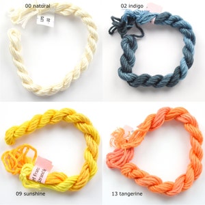 May include: Four skeins of embroidery floss in different colors: natural, indigo, sunshine, and tangerine. Each skein is wrapped in a circle and labeled with the color name and number.