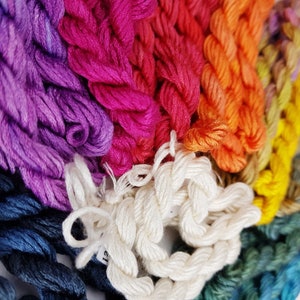 May include: A close-up of a variety of embroidery floss spools in different colors, including purple, pink, orange, yellow, and blue. The spools are arranged in a rainbow pattern. The floss is made of cotton and is suitable for hand embroidery, cross-stitch, and other needlework projects.