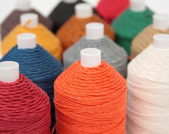 Könnte beinhalten: Eine Sammlung von Spulen mit farbigem Garn, darunter Rot, Orange, Gelb, Grün, Blau und Weiß. Die Spulen sind in einer Reihe angeordnet, wobei die rote Spule im Vordergrund steht.