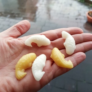 May include: A hand holding six small, colourful fish-shaped sweets. The sweets are white and yellow, and some have a glossy finish.