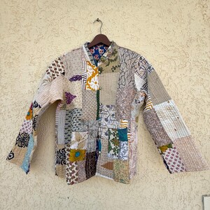 May include: A long-sleeved jacket featuring a patchwork design composed of various fabric squares with diverse patterns, including floral, geometric, and abstract prints in muted tones of beige, brown, blue, and yellow, with a button-front closure.