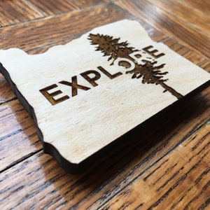 May include: Wooden cutout of the state of Oregon with a pine tree and the word "EXPLORE" engraved on it.