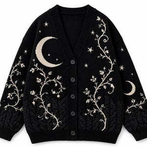 May include: A black V-neck button-down cardigan featuring a cream-colored knit pattern of crescent moons, stars, and winding vines. The lower portion of the garment displays a textured cable knit design in a matching black tone.
