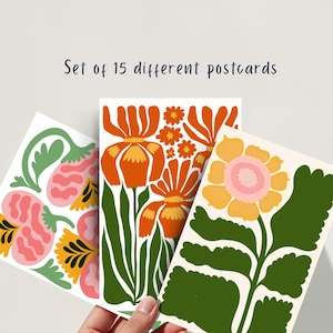 May include: A set of 15 different postcards featuring colorful floral designs. The postcards showcase various flowers in shades of orange, pink, yellow, and green. The text "Set of 15 different postcards" is displayed at the top.