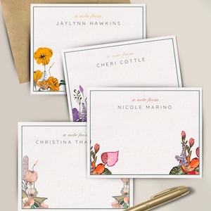 May include: Stationery set featuring personalized note cards with floral illustrations and the text "a note from" followed by names. Includes a kraft paper envelope and a gold pen. The cards have a white background with colorful flower designs.