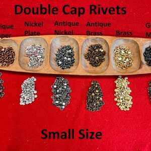 May include: An assortment of small double cap rivets in various finishes, including antique copper, nickel plate, antique nickel, antique brass, brass, and gun metal. The text "Double Cap Rivets" and "Small Size" are displayed.