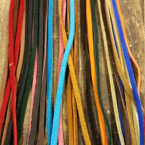K&ouml;nnte beinhalten: Eine Sammlung von Lederb&auml;ndern in verschiedenen Farben, darunter Rot, Blau, Braun, Orange und Gr&uuml;n. Die B&auml;nder sind vertikal angeordnet, wobei die Enden der B&auml;nder am unteren Rand des Bildes ausgerichtet sind.