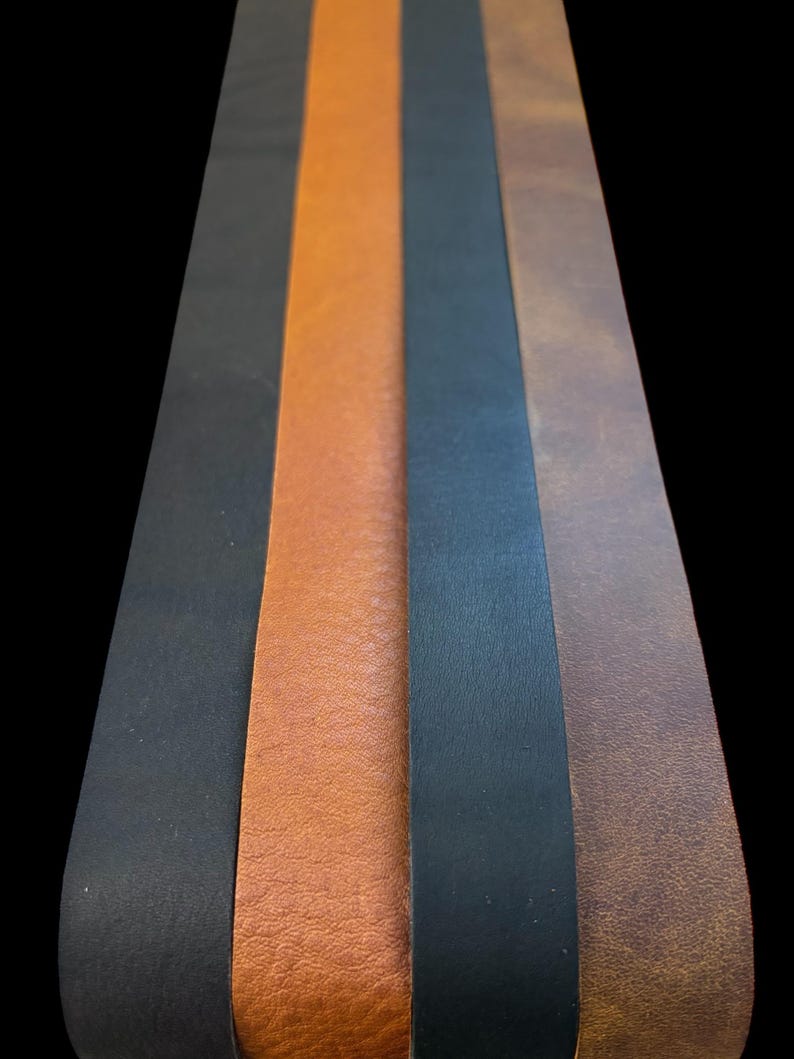 May include: Five leather strips in different colors and textures. The strips are arranged vertically, with the black strip on the left and the brown strip on the right. The strips are all about 1 inch wide.