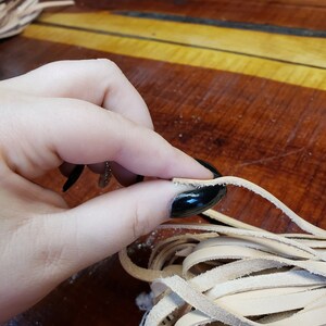 K&ouml;nnte beinhalten: Nahaufnahme einer Hand, die ein B&uuml;ndel hellbrauner Lederstreifen h&auml;lt. Die Streifen sind etwa 1,2 cm breit und haben einen leicht ausgefransten Rand.