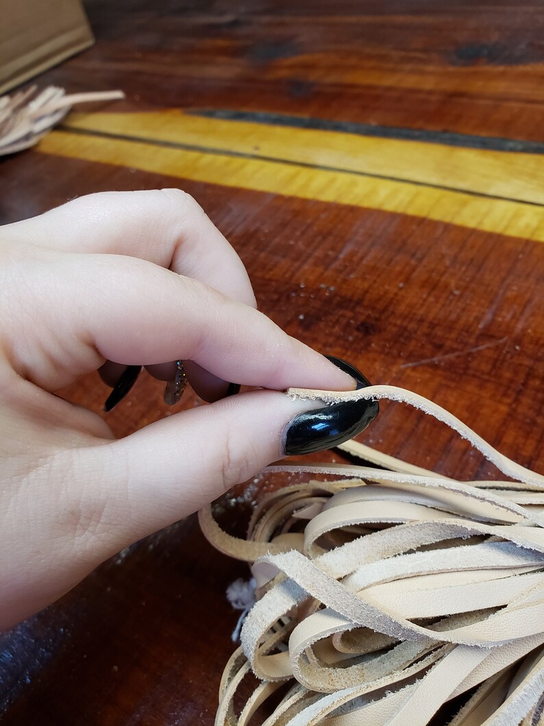 K&ouml;nnte beinhalten: Nahaufnahme einer Hand, die ein B&uuml;ndel hellbrauner Lederstreifen h&auml;lt. Die Streifen sind etwa 1,2 cm breit und haben einen leicht ausgefransten Rand.