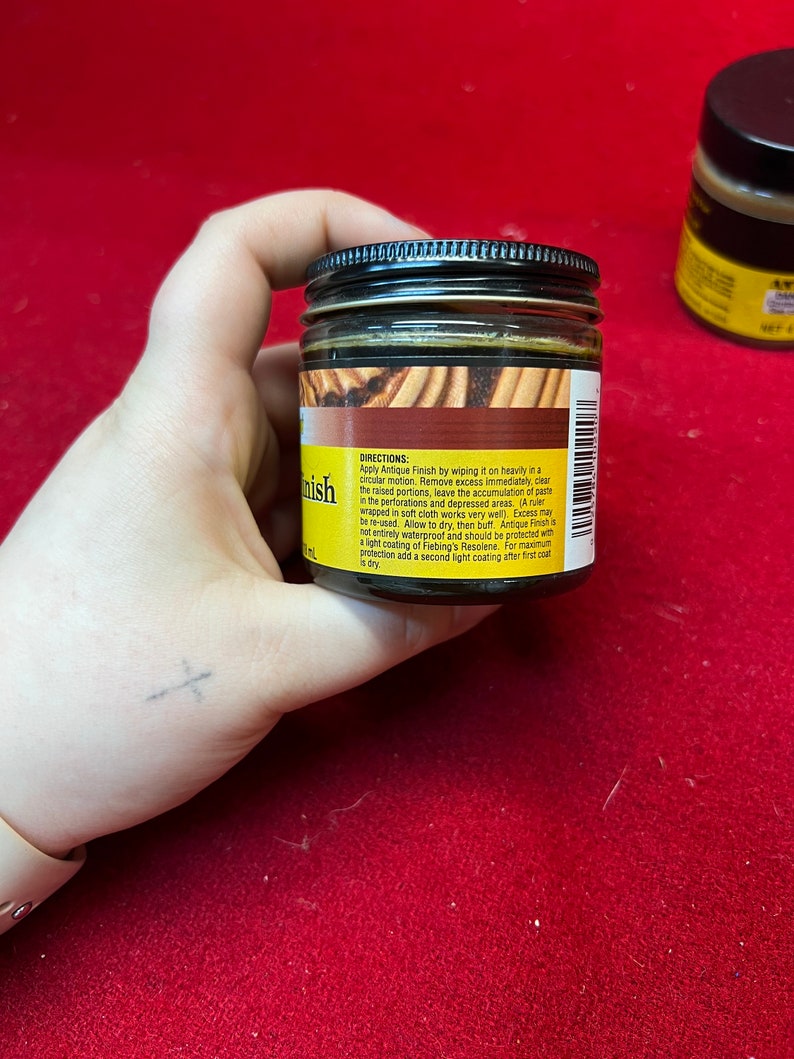 May include: A small glass jar of antique finish for leather. The jar is labeled with directions for use. The label reads: Apply Antique Finish by wiping it on heavily in a circular motion. Remove excess immediately, clear the raised portions, leave the accumulation of paste in the perforations and depressed areas. (A ruler wrapped in soft cloth works very well). Excess may be re-used. Allow to dry, then buff. Antique Finish is not entirely waterproof and should be protected with a light coating of Fiebing's Resolene. For maximum protection add a second light coating after first coat is dry.