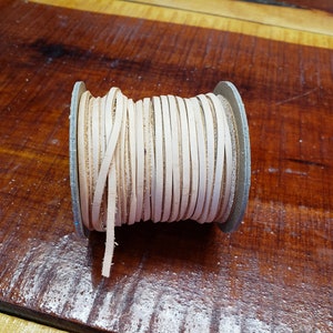 K&ouml;nnte beinhalten: Eine Spule mit off-wei&szlig;em Lederband, das um einen Kartonkern gewickelt ist. Das Band ist etwa 6 mm breit und eignet sich ideal f&uuml;r Lederbastelprojekte.