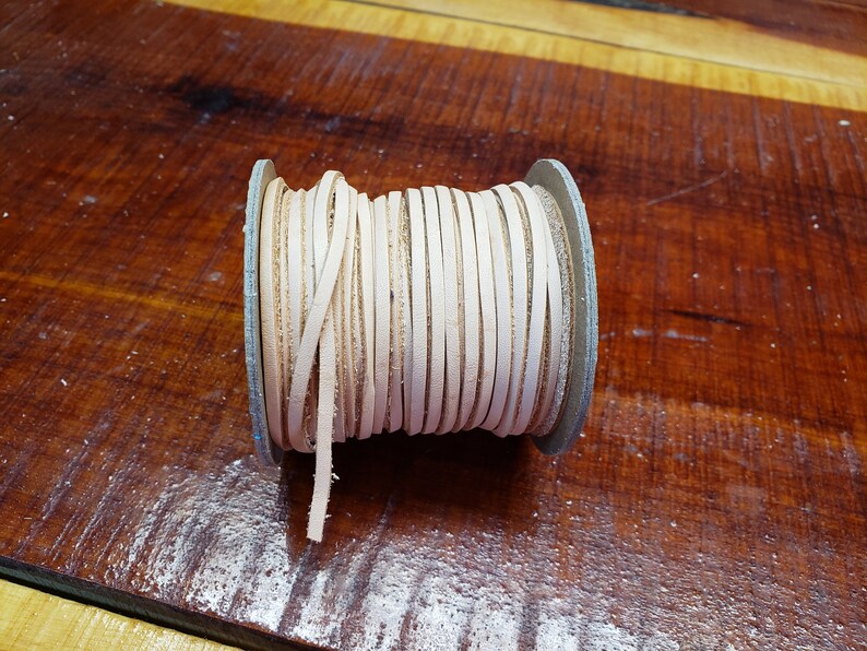 K&ouml;nnte beinhalten: Eine Spule mit off-wei&szlig;em Lederband, das um einen Kartonkern gewickelt ist. Das Band ist etwa 6 mm breit und eignet sich ideal f&uuml;r Lederbastelprojekte.