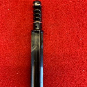 May include: Black plastic tool with a spring mechanism and silver rings. The tool is designed for crafting and has a long, rectangular handle.