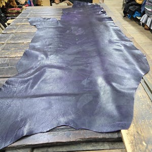 May include: A large piece of dark purple leather laid out on a wooden surface. The leather has a natural grain and a smooth, polished finish.