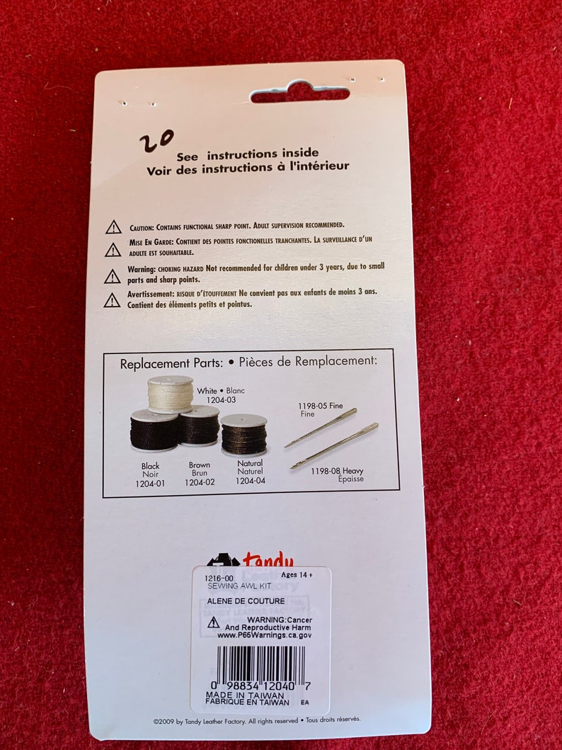 May include: A white and blue packaging for a sewing awl kit. The packaging includes a warning label about cancer and reproductive harm. The text on the packaging reads "Tandy Sewing AWL Kit" and "Alene de Couture". The packaging also includes a list of replacement parts with their corresponding numbers.