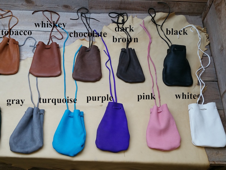 May include: Ten leather pouches in various colors, including tobacco, whiskey, chocolate, dark brown, black, gray, turquoise, purple, pink, and white. Each pouch has a drawstring closure and a long cord for carrying.