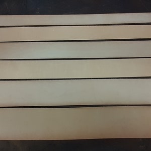 May include: Five strips of light brown leather, arranged horizontally, on a dark surface.