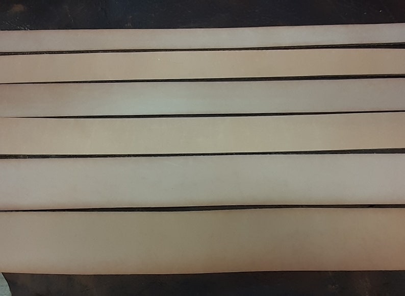 May include: Five strips of light brown leather, arranged horizontally, on a dark surface.