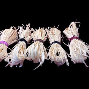 May include: Five bundles of natural, off-white, paper raffia ribbon tied with different colored string. The raffia is a flat, woven ribbon that is commonly used for crafts and floral arrangements.