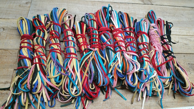 K&ouml;nnte beinhalten: Ein B&uuml;ndel bunter Lederb&auml;nder, die mit roter Schnur zusammengebunden sind. Die B&auml;nder sind in verschiedenen Blaut&ouml;nen, Gr&uuml;n, Gelb, Rosa, Rot, Orange und Braun.