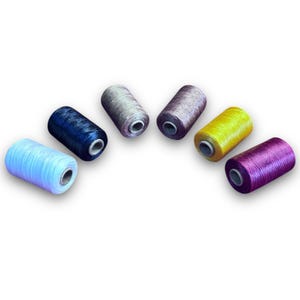 May include: Six spools of thread in various colors, including light blue, dark blue, gray, yellow, purple, and pink. The spools are arranged in a semi-circle on a white background.