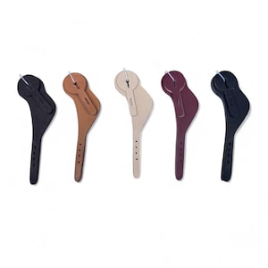 May include: Five leather stirrup leathers in various colors: black, brown, beige, burgundy, and dark navy. Each leather strap has a curved shape with a series of holes and a small loop at the top. The leathers are displayed against a white background.
