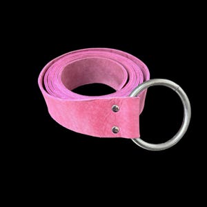 May include: A pink leather belt with a silver ring buckle. The belt is rolled up and the buckle is attached to the end of the belt.