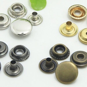 May include: Assortment of metal snap fasteners in silver, gold, and bronze finishes. The fasteners are in various stages of assembly, including caps, studs, and posts.