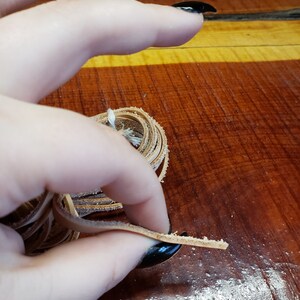 K&ouml;nnte beinhalten: Nahaufnahme einer Hand, die eine Spule mit hellbraunem Lederband h&auml;lt. Das Band ist etwa 6 mm breit und zu einem lockeren Kreis gewickelt. Die Hand h&auml;lt das Band in der Mitte der Spule, und das Band wird aus der Spule gezogen.