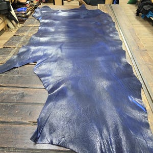 May include: A large piece of dark blue leather with a smooth, shiny surface. The leather is laid out flat on a wooden table.