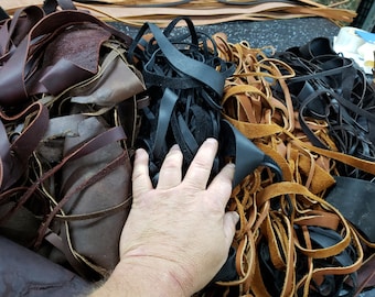 Könnte beinhalten: Ein Haufen Lederreste in verschiedenen Brauntönen, Schwarz und Beige. Das Leder ist in Streifen und Stücken, und einiges davon ist ausgefranst. Eine Hand liegt auf dem Haufen.