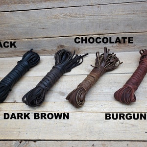 May include: Four spools of leather cord in different colors: black, dark brown, chocolate brown, and burgundy. The cords are arranged horizontally on a wooden surface.