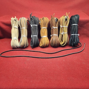 May include: Assortment of eight leather cords in various shades of brown and black, bundled together on a red surface.