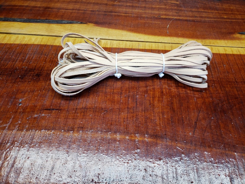 K&ouml;nnte beinhalten: Eine Rolle aus nat&uuml;rlichem Lederband, mit einem wei&szlig;en Gummiband zusammengebunden. Das Band ist etwa 6 mm breit und eignet sich ideal f&uuml;r Lederbastelprojekte.