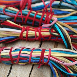 K&ouml;nnte beinhalten: Ein B&uuml;ndel bunter Lederkordeln, die mit roter Schnur zusammengebunden sind. Die Kordeln sind in verschiedenen Blaut&ouml;nen, Gr&uuml;n, Gelb, Rosa, Rot und Braun.